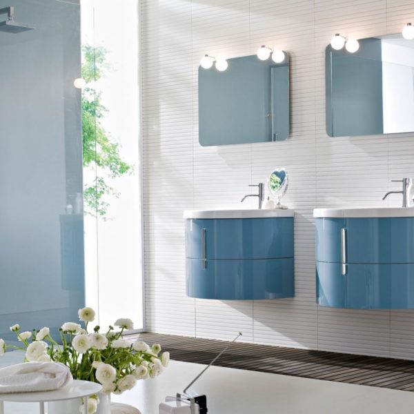 Ein Gäste-WC mit einer modernen Badezimmereinrichtung der IDEA-GROUP-Serie Moon. Das Waschbecken ist aus Keramik und hat eine gebogene Form. Der Spiegel ist ebenfalls aus Keramik und hat eine runde Form. Die Schränke sind aus Holz und haben eine matte Oberfläche. Die Farbe der Einrichtung ist weiß.